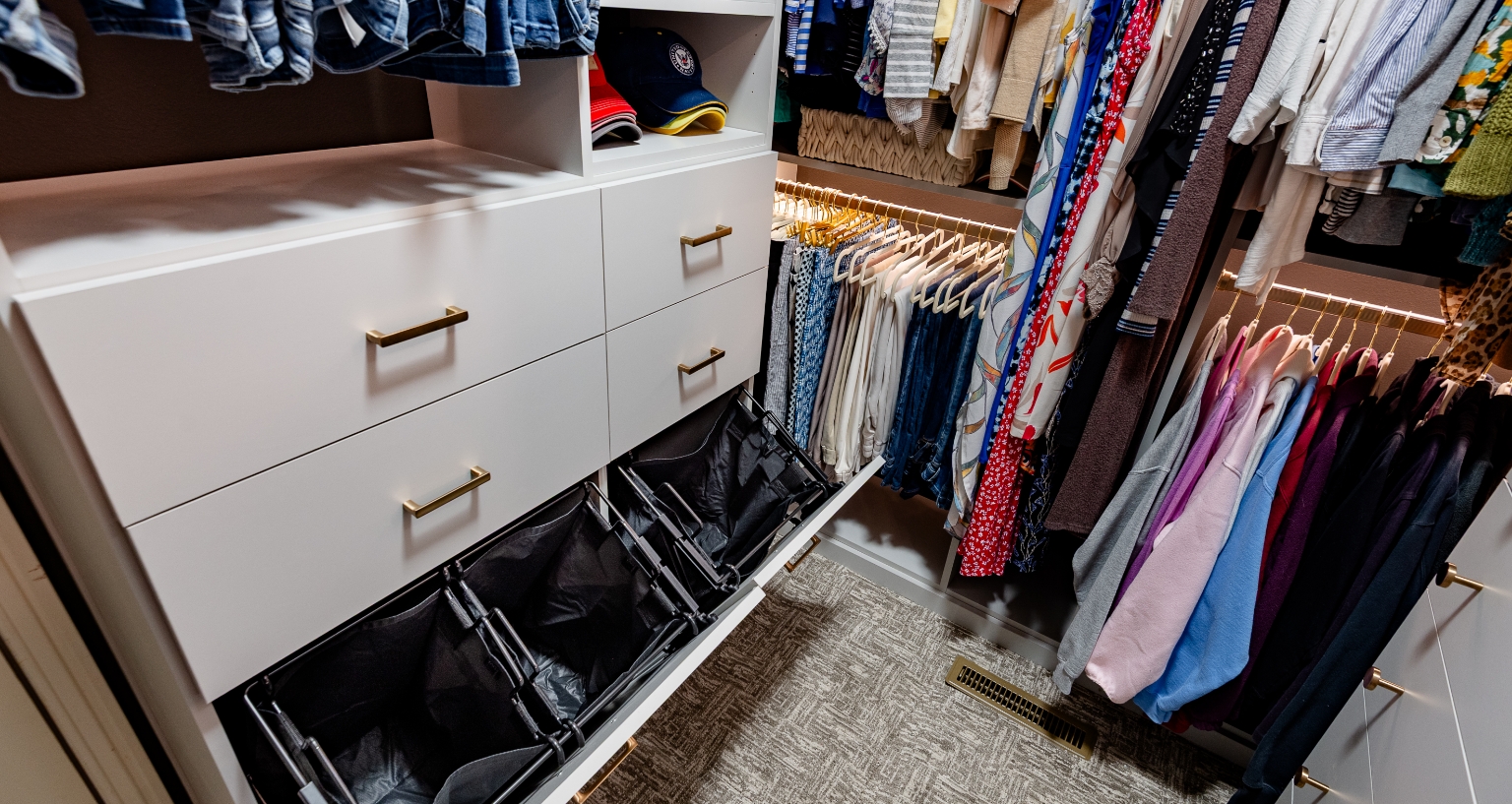 Smaller walk-in closet with organized beauty featuring clothes hampers